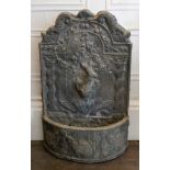 A weathered lead water fountain, after the antique, the shaped arched back surmounted by dolphins,