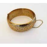 A 9ct gold hollow bangle of oval form, engraved to one side with repeat flowerheads and foliage,