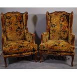A pair of 20th century French stained beech wingback armchairs on cabriole supports,
