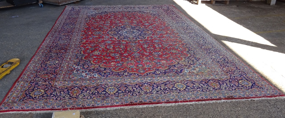 A Kashan carpet, Persian, the madder field with a bold indigo medallion, matching spandrels,