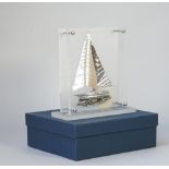 A silver model of a Greek yacht, in sail with rigging, displayed in a perspex stand,