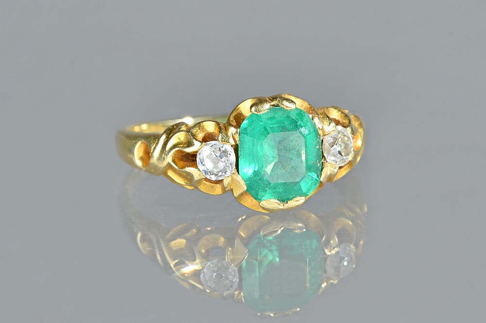 A gold, emerald and diamond set three stone ring, mounted with the step cut emerald at the centre,