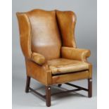 A George III style tan leather upholstered wingback armchair on block mahogany supports,