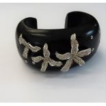 An ebonised hardwood and diamond set torc bangle, set with three graduated flowerheads,