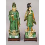 A pair of Chinese pottery figural roof finials, polychrome painted, each on a wooden stand,