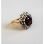 A gold, ruby and diamond set oval cluster ring, collet set with the oval cut ruby at the centre,