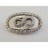 A white precious metal and diamond set brooch, of oval design, the central diamond set S motif,