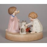 A Russian biscuit porcelain figure group of two small children and a cat drinking milk from a bowl,