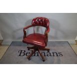 A 20th century stained beech office swivel open armchair with red leather button back upholstery,