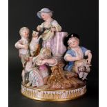 A Meissen group of five children gathered around a rocky mound with a classical column,