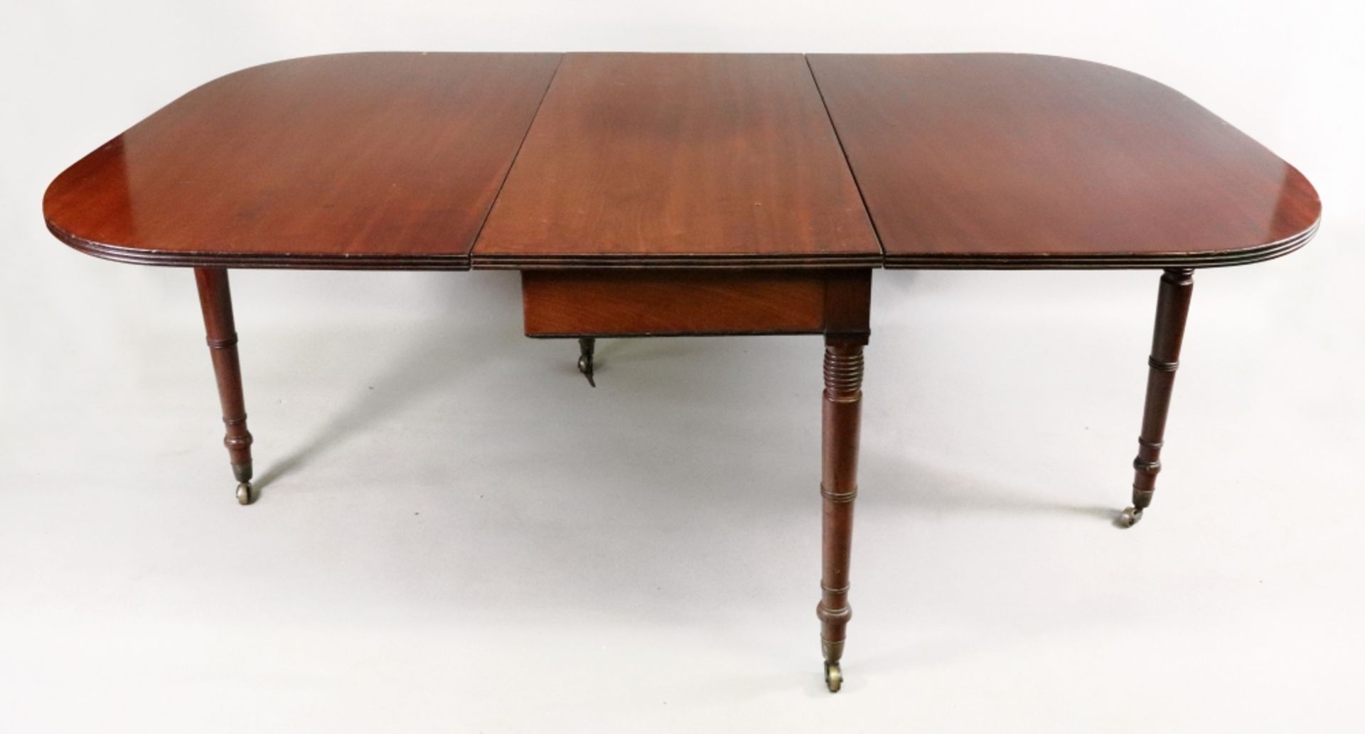 A George III mahogany drop leaf dining table, the deep hinged rounded leaves with reeded edge,