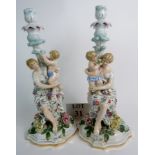 A pair of German porcelain candlesticks with figural and floral decoration, 31cm tall,