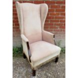 A slim early 20th century mahogany framed high back winged armchair upholstered in a peach material,