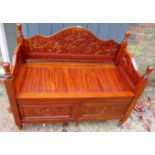 A 20th century carved settle with a lift up seat revealing an internal storage compartment,