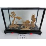 A carved cork Oriental landscape in a glass case showing an incredible level of detail: trees,