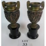 A pair of bronzed urns in the classical style with Roman figures in relief, (slightly a/f),