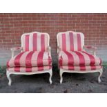 A pair of painted 20th century French open sided low armchairs with loose seat cushions,