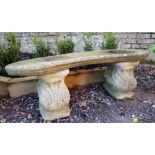A stone garden bench with a curved seat over decoratively carved seat,