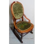 A Victorian carved rocking chair with a green velvet upholstered back and seat pad over turned legs