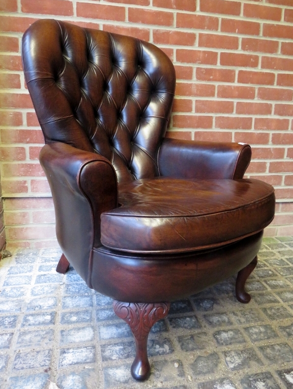 A 20th century brown backed brown leather armchair with a loose seat cushion over carved cabriole