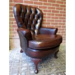 A 20th century brown backed brown leather armchair with a loose seat cushion over carved cabriole