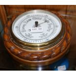 AN ANEROID BAROMETER mounted within a circular oak wall case with rope twist carved rim, dial 16cm