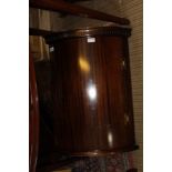 A REPRODUCTION MAHOGANY COLOURED HANGING BOW FRONT CORNER CUPBOARD