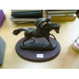 A CAST MODEL OF A RACE HORSE WITH JOCKEY UP, standing on an oval wooden plinth