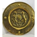 AN EMBOSSED BRASS WALL PLAQUE, to the centre a Heraldic device, with lion supporters, 58cm diameter