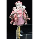 AN EARLY 20TH CENTURY COMBINATION DOLL WITH WHISTLE HANDLE, having a bisque head and pink fabric