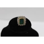 AN EMERALD AND DIAMOND RING, the rectangular cushion cut central emerald surrounded by a border of