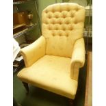 AN OLD GOLD UPHOLSTERED BUTTON BACKED DEEP SEATED ARMCHAIR on turned fore legs and plain rear