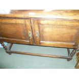 AN OAK LOW SIDEBOARD UNIT with two plain cupboard doors, supported on barley twist and blocked