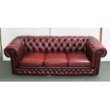 A RED LEATHER THREE SEATER CHESTERFIELD SOFA, having buttoned and studded upholstery