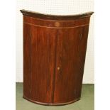 A GEORGIAN MAHOGANY BOW FRONTED CORNER CUPBOARD having decorative inlaid stringing and plain