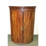 A 19TH CENTURY MAHOGANY BOW FRONTED CORNER CUPBOARD with decorative quarter fan inlay, opening to