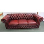 A RED LEATHER THREE SEATER CHESTERFIELD SOFA, having buttoned and studded upholstery, with seat