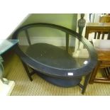 A BLACK ASH FRAMED OVAL INSERT GLASS TOPPED COFFEE TABLE with solid magazine undertier