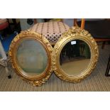 TWO OVAL PLAIN PLATE WALL MIRRORS in foliate carved gilded frames