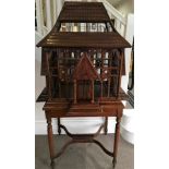 A mahogany Victorian style bird house with tiled effect roof sitting on a four turned leg base.