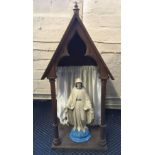 A painted figurine of the Virgin Mary housed in a wooden structure with satin curtain. Height 81cm.