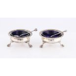 A pair of Victorian silver salts, both of circular design raised on three claw feet, with blue glass