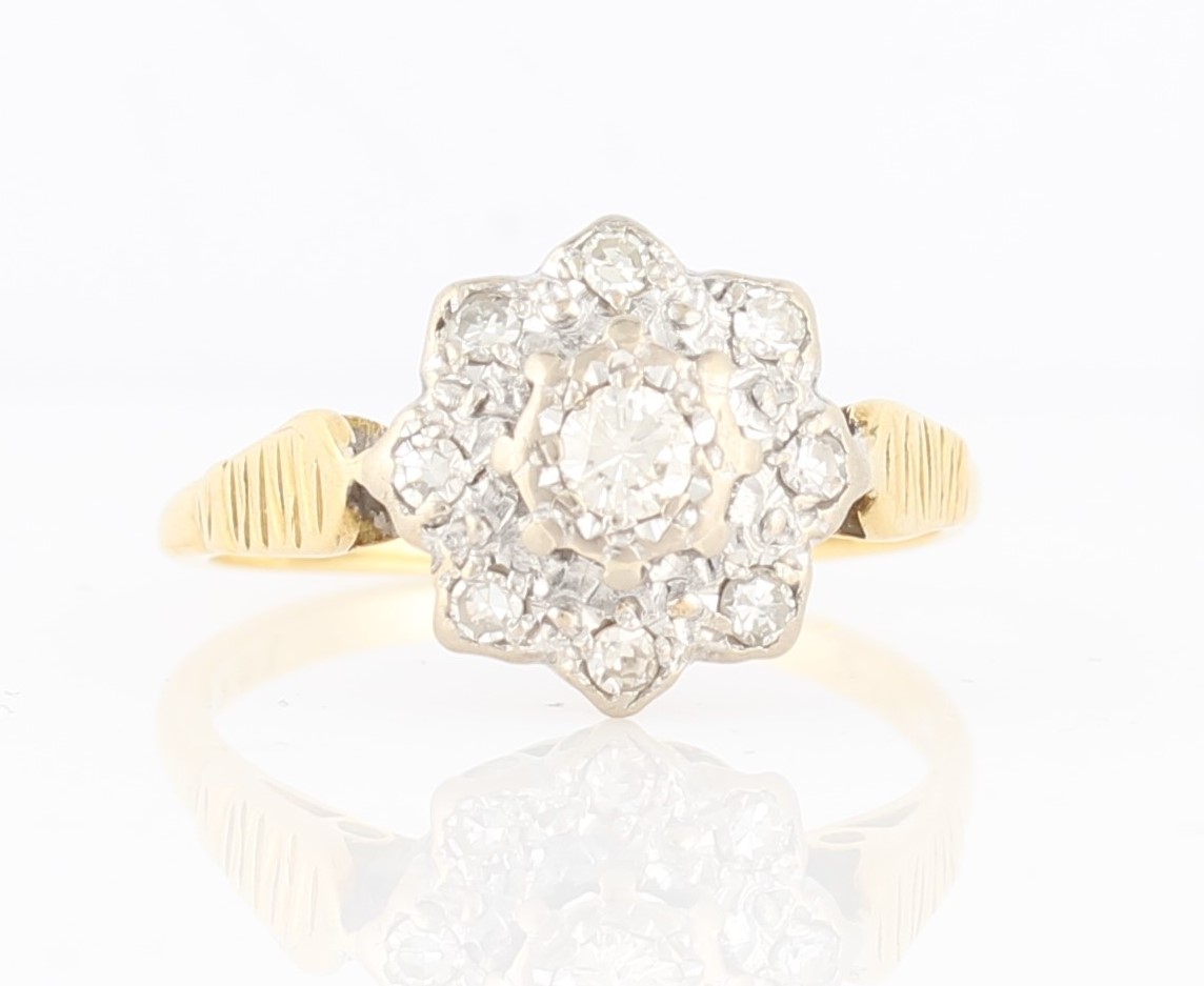 A diamond set flower design ring, set with a central round brilliant cut diamond, measuring