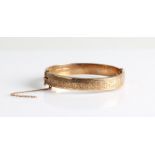 A hallmarked 9ct yellow gold engraved hinged bangle, (safety chain A/F).