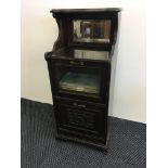 A stained walnut glazed front music cabinet with one pull down cupboard door.