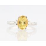 A yellow beryl / heliodor and diamond three stone ring, set with a central oval cut heliodor,