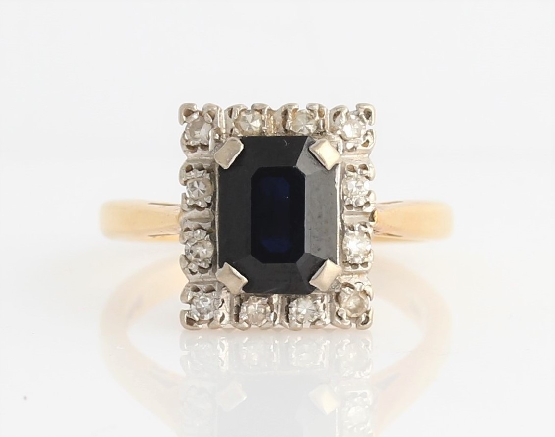 A hallmarked 18ct yellow gold sapphire and diamond cluster ring, set with an emerald cut sapphire