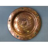 An Arts and Craft style hand beaten copper plate, with female profile to centre and green glass