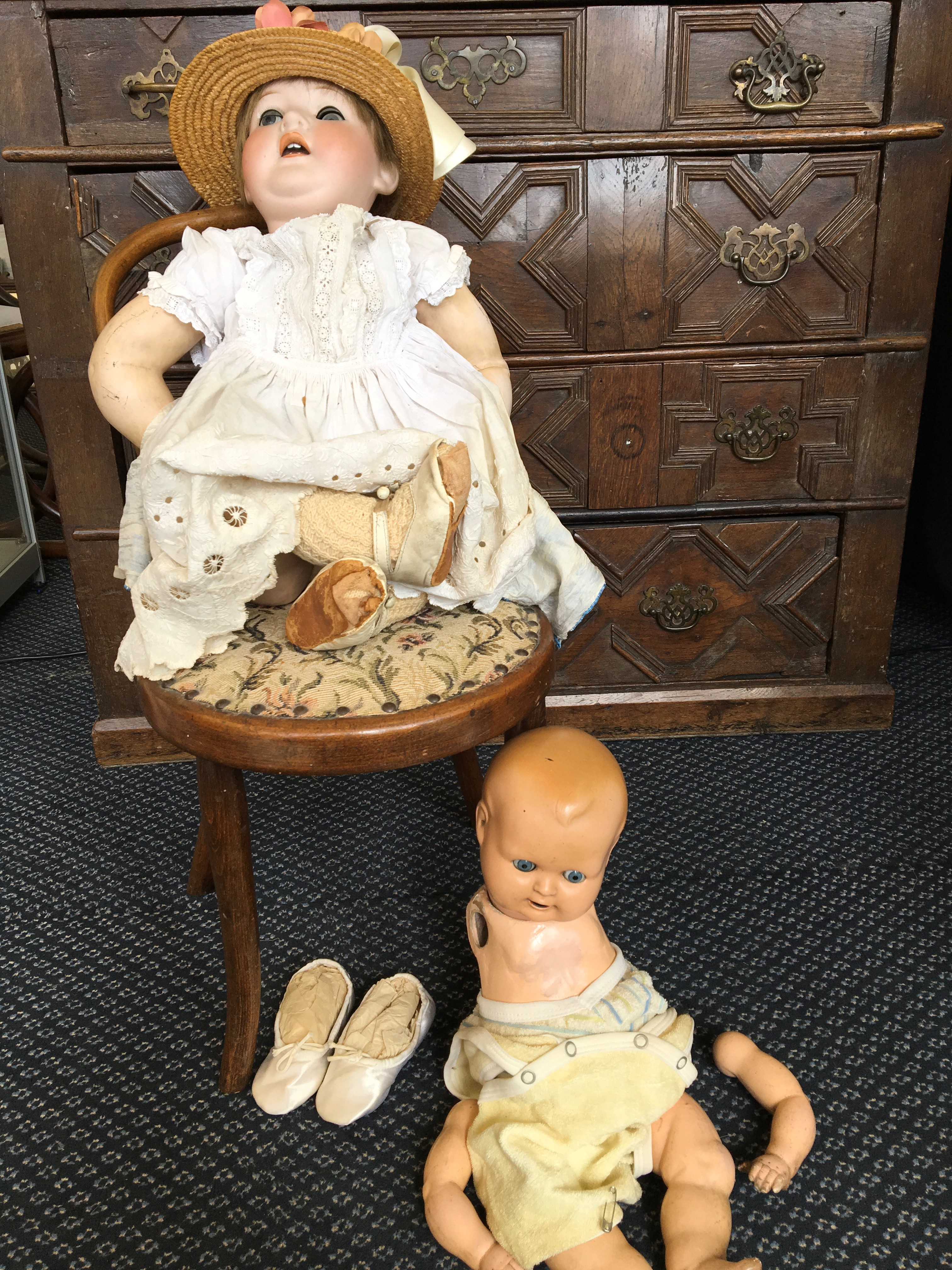 Two dolls, one porcelain-faced with hat and christening dress, with chair.