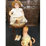 Two dolls, one porcelain-faced with hat and christening dress, with chair.